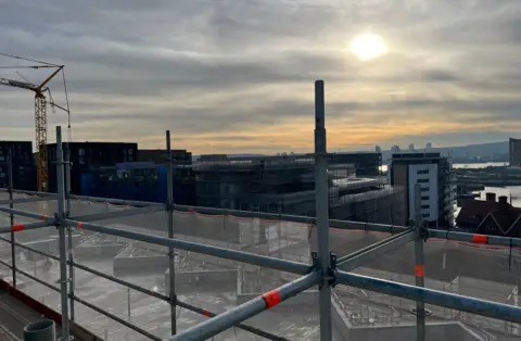 BBC/Harry Low Building scaffolding overlooking another building site with Thames and sun in background