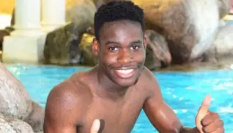 Family handout A young man smiling with his thumbs up. He is topless and there is a swimming pool behind him, with some rocks along the side of it.