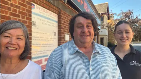 Chris McHugh / BBC From left to right: Ping Low, wearing a white t shirt and with shoulder length black hair, Barry Allday, wearing a smart white checked shirt with long brown hair, and Sarah Windsor, wearing a blue polo shirt and tied back long brown hair
