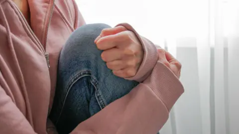 Getty A close up of a woman's legs while she it sitting down wearing jeans and a pink jumper 