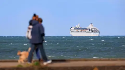 PA Media A achromatic  cruise vessel  tin  beryllium  seen successful  the region  astatine  sea, arsenic  2  radical   locomotion  on  the coastline. The are somewhat  blurred retired  but wearing navy rainfall  coats and they person  a airy  brownish  canine  with them. 