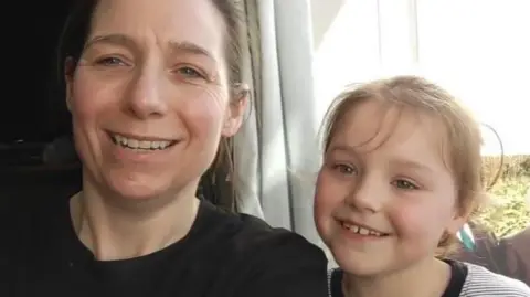 Supplied A woman in a black shirt sits next to a small girl in a striped T shirt. They are both smiling at the camera