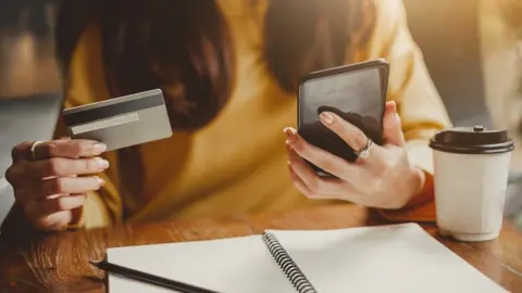 Getty Images Woman looking at mobile phone and credit card