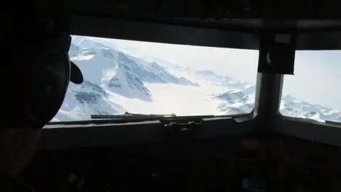 Gregory Ng From the cockpit of the plane: a chain of snowy mountains with an ice-filled valley in between