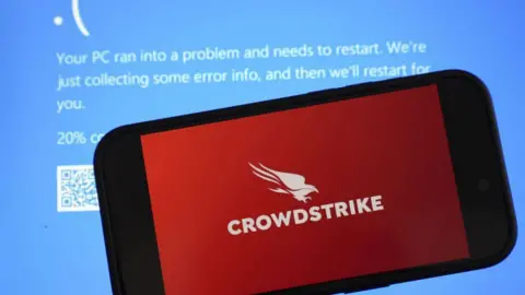 맹금류의 빨간색 CrowdStrike 로고가 있는 전화기가 파란색 오류 메시지를 표시하는 PC 화면 앞에 놓여 있음