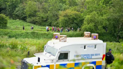 Pacemaker A police van in the foreground, with walkers in the background. There is lots of greenery.