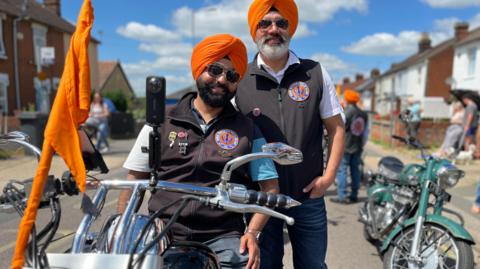 Two Sikh men, wearing orange turbans, on motorcycles