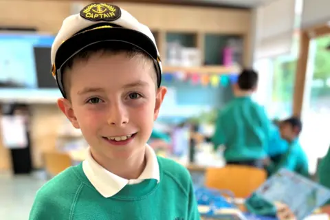 Young boy in school uniform and a sailor's hat smiling at camera