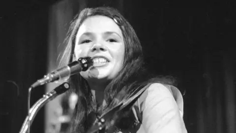 Getty Images Black and white picture from December 1971: Pop singer Dana (born Rosemary Brown now Dana Rosemary Scallon), who won the 1970 Eurovision song contest with 'All Kinds of Everything'. She has long hair, singing in front of a microphone.