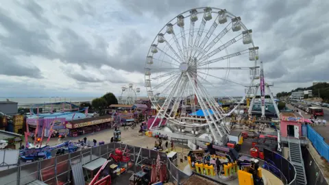 A photo of Adventure Island in Southend-on-Sea, with a large ferris wheel and several rollercoasters and other amusements. There is cloudy sky overhead