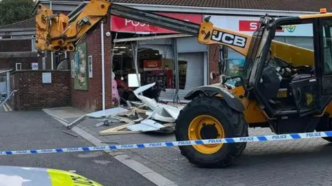 Ben Luke A yellow JCB digger in front of shop with a smashed up window and police tape around the scene 