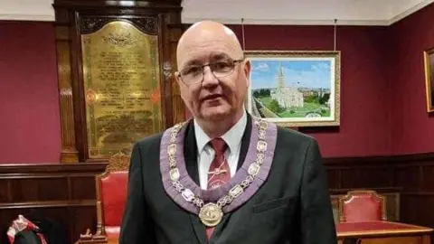 ABOD William Walker dressed in a suit and wearing a chain and floret. 