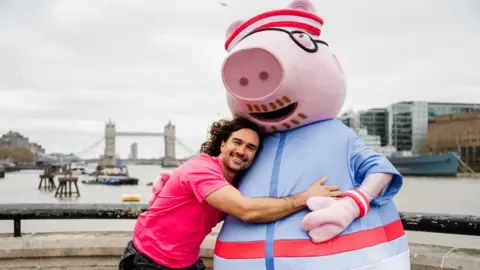 Charlie Flint/PA Wire Joe is wearing a pink T-shirt and has his arms around Daddy Pig who has a pink head and hands, and a blue and pink shirt.