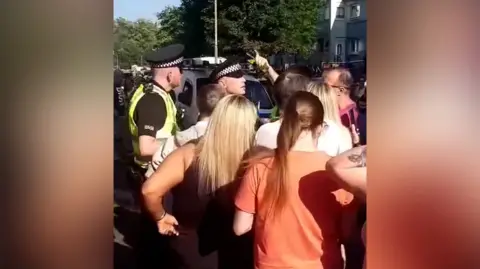 Video grab of two police officers talking to a group of people who are pictured from behind