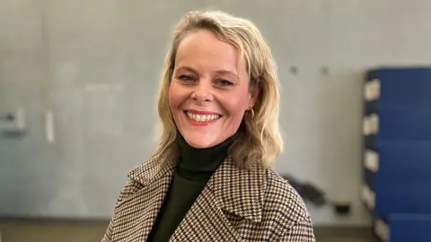 Sam Read/BBC A head and shoulders photo of Jane Bethea. She is looking at the camera and smiling. Behind her the background is blurred, but it shows a concrete wall, with a pile of blue crates visible to the left of the picture.
