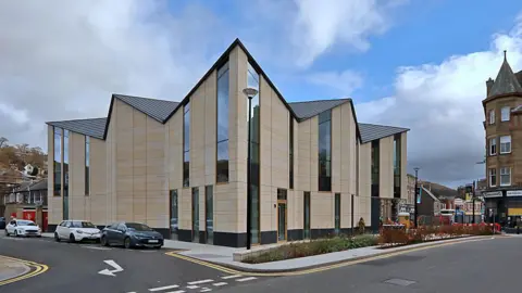 Walter Baxter The Great Tapestry of Scotland visitor centre - a spikey-roofed building in the heart of Galashiels with cars parked outside and some planting in front of it
