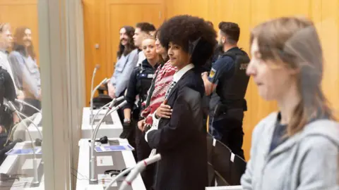 Activists behind glass in the high security prison courtroom. Standing in front of microphones hand cuffed. 