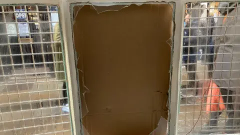 A close-up of a smashed window pane, boarded up with cardboard.