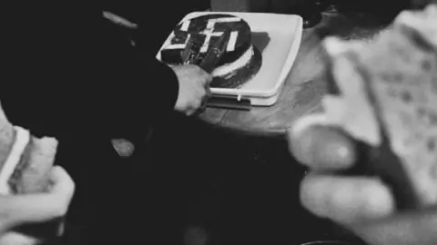 Telegram Active Club members cut into a cake decorated with a swastika and grab slices of it