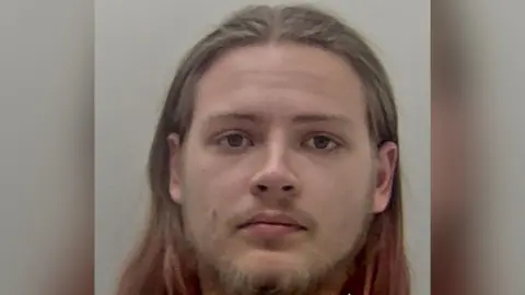 Kent Police A mugshot of a man with long hair and a beard.