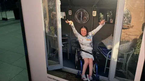 A woman in a wheelchair has her arms in the air waving on a board