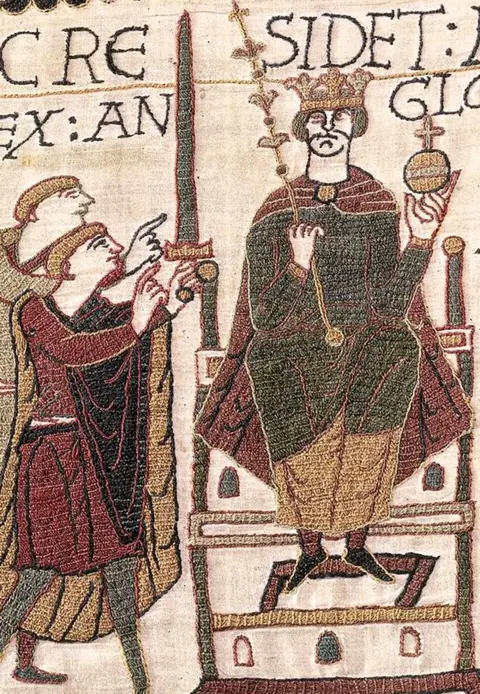Bayeux Museum A close crop of the same scene, centred on Harold sitting on the throne holding an orb and stick along with figures to his left, with medieval lettering and fabric texture detail.