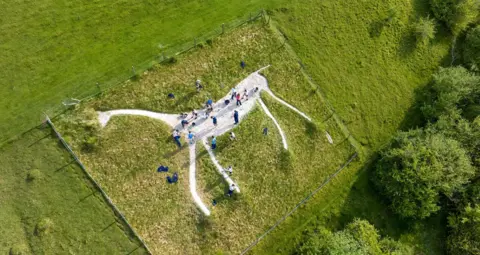 Marlborough College An aerial view of a slim white horse with people on top of it.