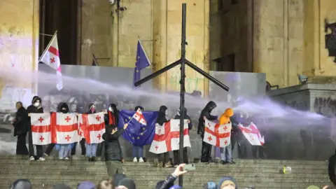 Getty Images Protesters in Georgia stand outside parliament and are doused with water cannon