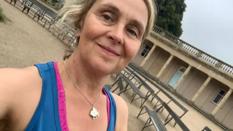 Katie Treutler Katie Treutler, wearing a blue running vest, smiles at the camera in a selfie taken in Eaton Park, Norwich, with park buildings and benches behind her.