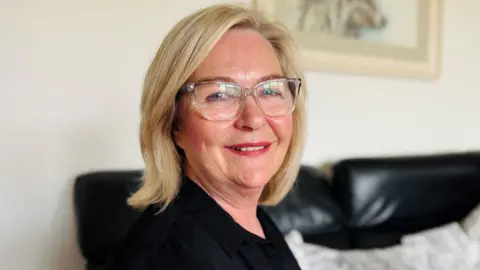 Brenda Young, a woman with shoulder length blonde hair and glasses smiling at the camera.