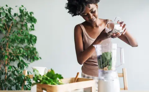 Getty Images Stock photo shows a woman adding chia seends into a smoothie at home, there is a plant in the background.