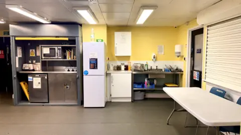 His Majesty’s Inspectorate of Probation An industrial-type kitchen with yellow walls and the window shutters down
