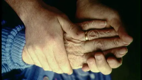 Elderly person holding hands with a helper.