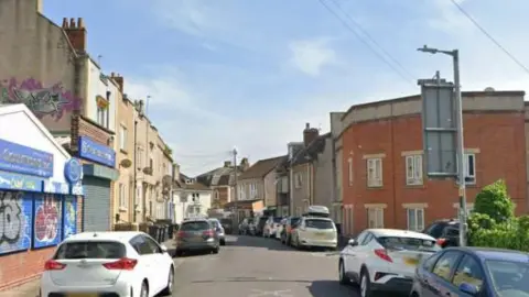 A Google Maps screengrab of Oxford Place in Easton, Bristol, a narrow residential street lined with parked cars with a garage on the corner. 
