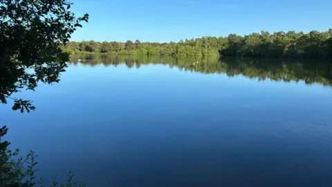 Jake Zuckerman/BBC A serene, calm lake under a blue sky.