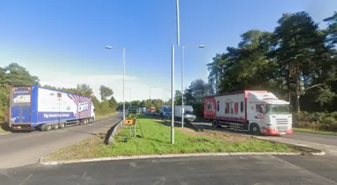 Two lorries by a roundabout, showing roads signs, street lights