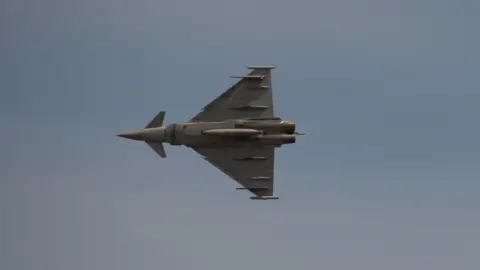 The picture is taken right beneath the aircraft, which is shaped like a dart with an arrow head at the front. On its belly, it holds various missiles.