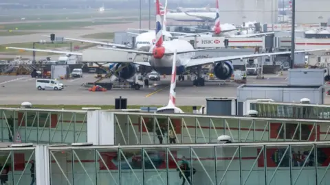 Getty Images A general view of Heathrow Airport, with glass walkways showing passengers walking and planes on a runway.