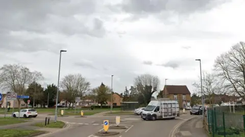 Google A roundabout where St Paul's Road, Peterborough, meets Dogsthorpe Road (straight ahead) and Welland Road (on the left). There are vans and cars using the road. On either side are pavements and lamp posts. 