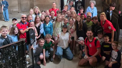 Masefield Primary School Singer Jessie J wears white t-shirt, blue jeans and dark cap as she poses with the large group of schoolchildren.