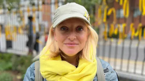 BBC/Harry Low Emma Semp wearing baseball cap with yellow ribbon on and yellow scarf