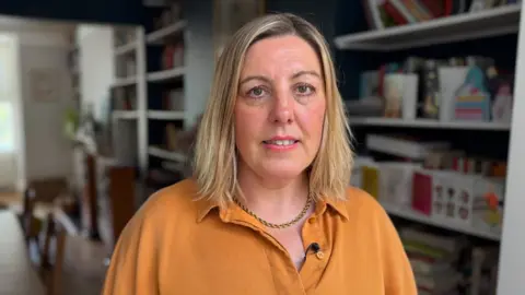 A portrait image of Rachel Cashman, the co-founder of PSHE Brighton staring straight at the camera. She has shoulder length blonde hair and is wearing a yellow shirt.