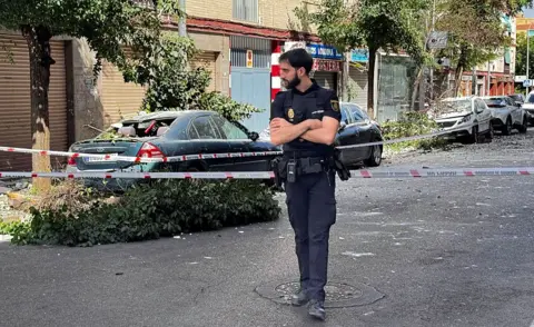 AFP via Getty Images A policeman stands at a cordoned off street near damaged vehicles following an earthquake in Granada, southern Spain. Photo: 18 August 2026