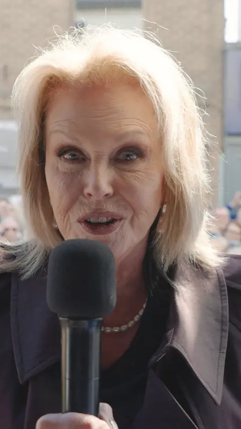 Joanna Lumley stood in front of a camera with a black microphone wishes Sir David Attenborough a happy birthday