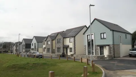 A line of smart, newly-build house, with a green space in front and a part-finished tarmac road.