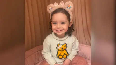 Lauren Griffin A toddler smiling at the camera wearing a beige jumper with Pudsey on the front