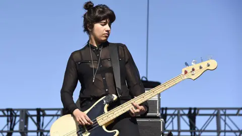 Getty Images Ayse Hassan, onstage at an outdoor festival playing her bass. She is wearing all black, with the top partly see-through. 