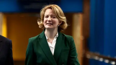 Getty Images A woman with medium length blonde hair in a green suit. 