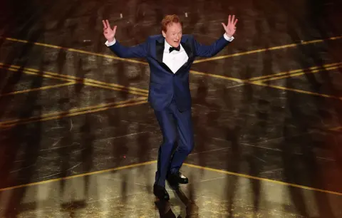 Getty Images  Conan O'Brien jumps with his hands in the air while hosting the 98th  Academy Awards.