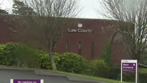 A picture of the outside of Magistrates court in Bodmin. It is a brick building with a silver sign outside the front of it. 